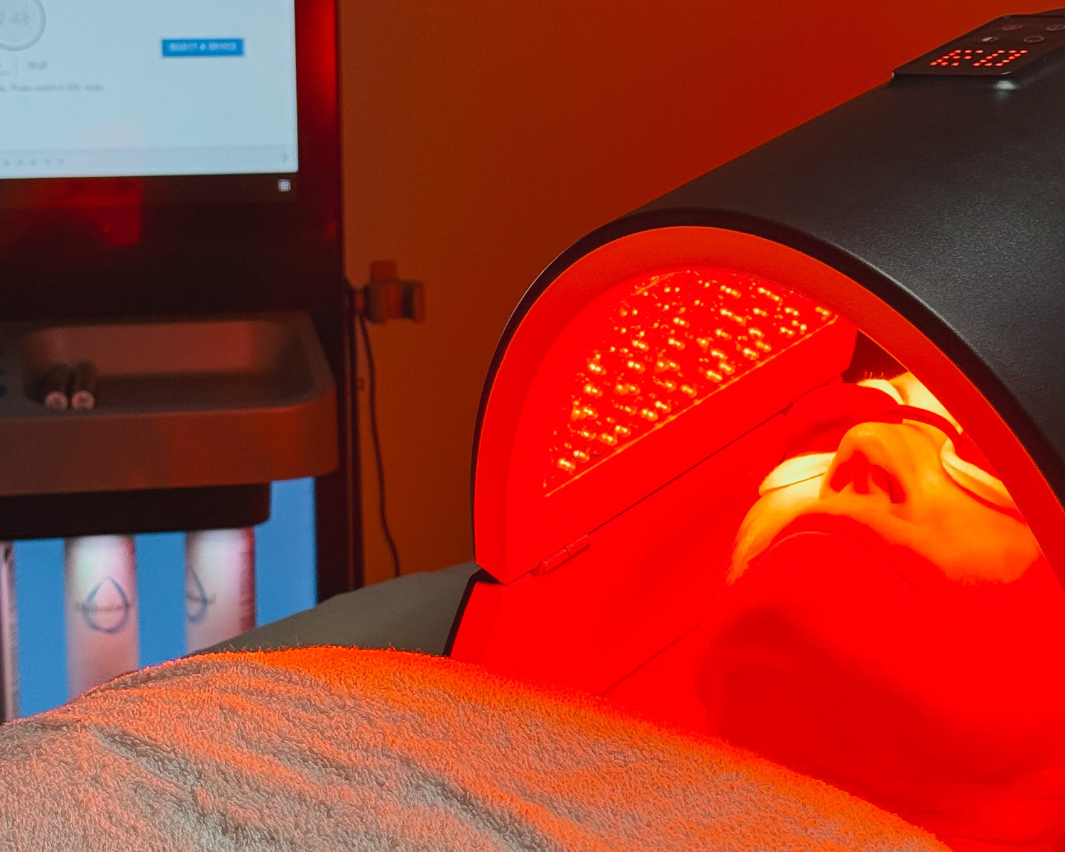 Person receiving red light therapy with a device and computer monitor in the background.